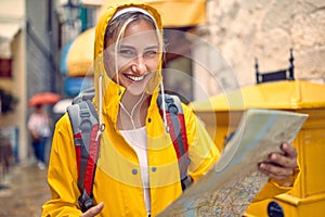 Girl with a yellow raincoat and map on the street while enjoying a walk through the city on a rainy day