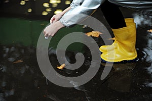 A girl in a yellow rubber boots walks through the forest. Travel concept with children. Autumn in the forest.