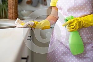 The girl in yellow rubber gloves and an apron removes. Hand wipes the table surface and holds the spray