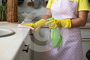 The girl in yellow rubber gloves and an apron removes. Hand wipes the table surface and holds the spray