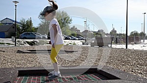 A girl in yellow shertas and a white T-shirt jumps on a trampoline on the street in the early summer morning