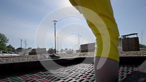 A girl in yellow shertas and a white T-shirt jumps on a trampoline on the street in the early summer morning on a children`s playg