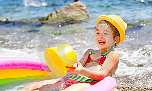 Girl in yellow straw hat plays with the wind, water and a water dispenser in an inflatable pool on the beach. Indelible products