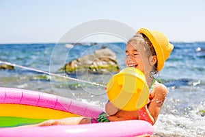 Girl in yellow straw hat plays with the wind, water and a water dispenser in an inflatable pool on the beach. Indelible products