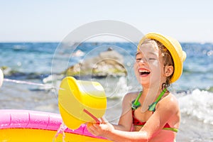 Girl in yellow straw hat plays with the wind, water and a water dispenser in an inflatable pool on the beach. Indelible products