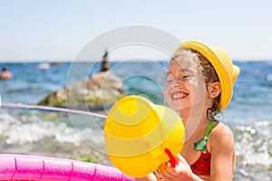Girl in yellow straw hat plays with the wind, water and a water dispenser in an inflatable pool on the beach. Indelible products