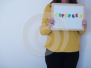 Girl in yellow sweater holds white board with the word asperger. asperger syndrome health concept