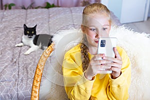 Girl in yellow sweatshirt looking at screen of mobile phone, holding it in hands