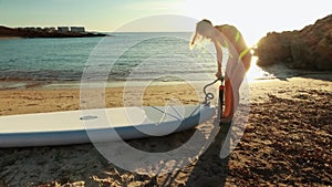 a girl in a yellow swimsuit pumps up her SUP against the backdrop of the sea. A close-up shot