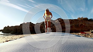 a girl in a yellow swimsuit pumps up her SUP against the backdrop of the sea. A close-up shot