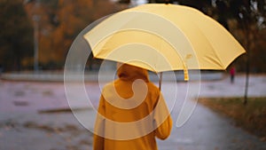 girl with yellow umbrella Slow motion rain city park. young woman hiding under umbrella from raindrop. walk slush