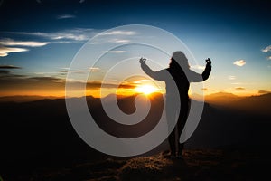 Girl in yoga meditation on top of a mountain at sunset