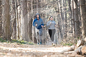 Girl and young man wearing sportswear and running in forest at m