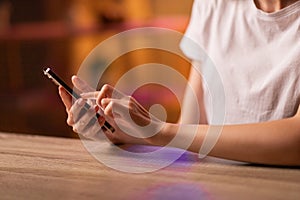 A girl or young woman sits at the table, holds in hands and uses a smartphone to correspond, read and send messages photo