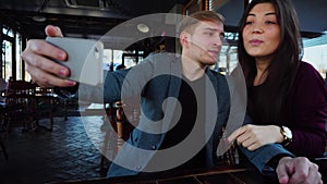 Girlfriend and boyfriend sitting in cafe taking selfie with smartphone.