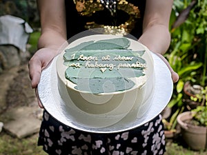 Girlfriend handing over a small cake with green icing and a heartwarming message. Tagalog words translated as 1 year and forever. photo