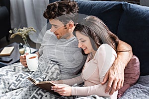 Girlfriend reading book and boyfriend holding cup of tea