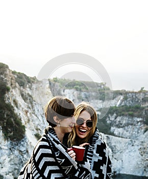 Girlfriends cuddle together under blanket on top of the mountain