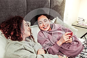 Girlfriends feeling relaxed while lying in bed and having conversation