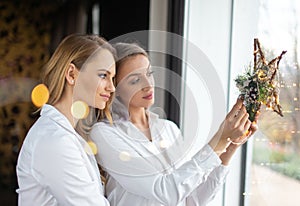 Girlfriends holding Christmas star decoration in window with fairy lights