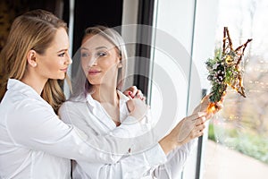 Girlfriends holding Christmas star decoration in window looking to each other