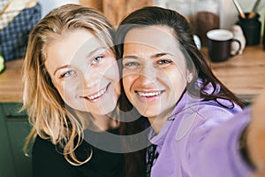 Girlfriends laugh merrily and take selfies in the kitchen.