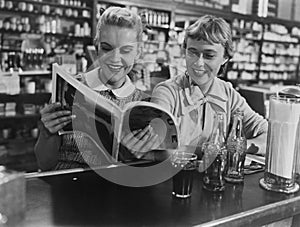 Girlfriends looking at magazine at soda fountain photo