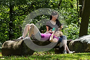 Girlfriends at park using smartphone and tablet, horizontal