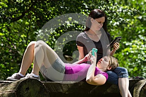 Girlfriends at park using smartphone and tablet, horizontal