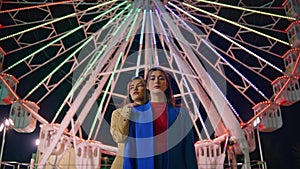 Girlfriends posing ferris wheel at night. Two models resting illuminated funfair
