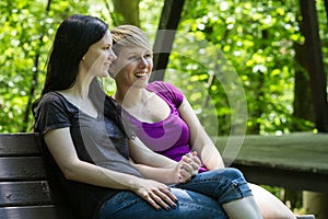 Girlfriends sitting on park bench holding hands, horizontal