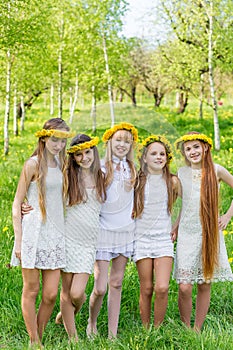 Girlfriends are standing with wreaths of dandelions on their heads in the open air