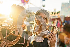Girlfriends together on a Bavarian fair or oktoberfest or duld in national costume or Dirndl eating pretzel or brezen