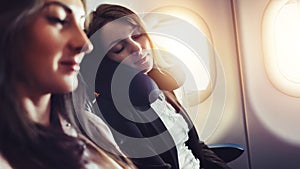 Girlfriends traveling by plane. A female passenger sleeping on neck cushion in airplane.