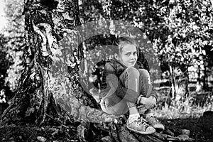 Girlie sitting on the roots of a birch. Black and white photo.