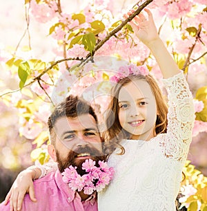 Girlish leisure concept. Girl with dad near sakura flowers on spring day. Father and daughter on happy faces hugs