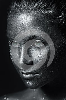 The girll`s beautiful face is painted silver with sequins. shiny metal powder particles sparkle on the model`s face
