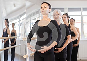 Girls in ballet class perform first position with participation of mature female mentor