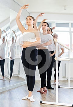 Girls in ballet class perform forth position with participation of mature female mentor
