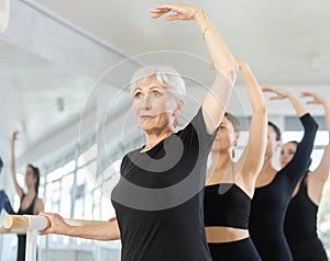 Girls in ballet class perform third position with participation of mature female mentor