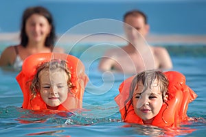Girls bathing in lifejackets with parents in pool