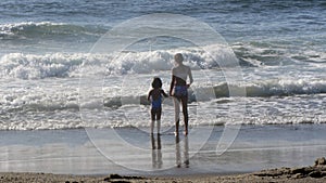 Girls on the beach in front of waves holding hands waiting to jump the waves