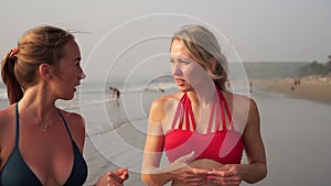 Girls in bikinis on the sea. Two young women girlfriends are walking along the beach