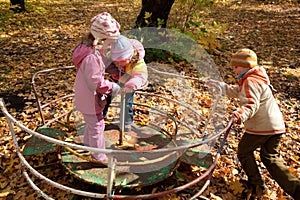 Girls and boy play on roundabout in autumnal park