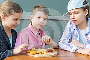 Girls and a boy sitting at a table and eating fast food, nuggets with sauce and French fries