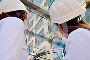 Girls in building white helmets with tablets in hands on the background of a glass office building.