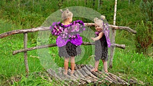 Girls with butterfly wings stand on wooden bridge