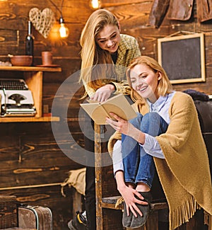 Girls with cheerful faces laughing about funny moment in book. Mom and daughter reading together on cold winter evening