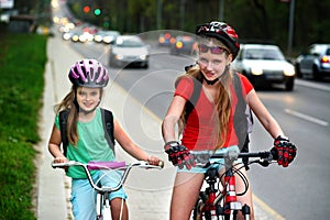 Girls children cycling on yellow bike lane. Cars are road.