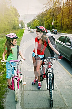 Girls children cycling on yellow bike lane. There are cars on road.